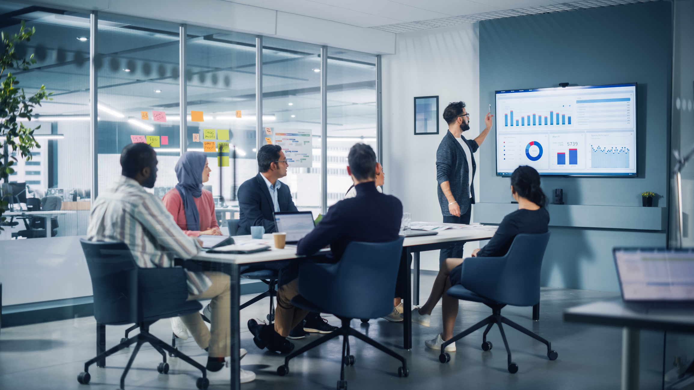 Diverse Modern Office: Motivated Latin Businessman Leads Business Meeting with Managers, Talks about Company Growth, Uses TV for Presentation. Creative Digital Entrepreneurs Work on e-Commerce Project